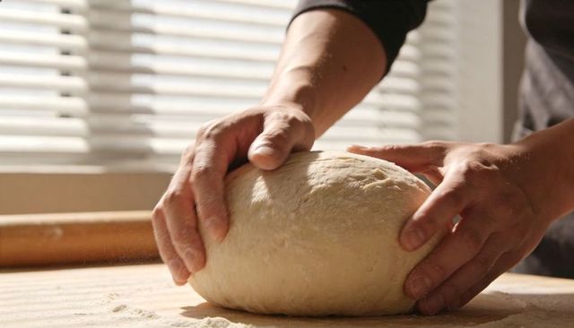 Shaping rustic bread dough with hands on floured counter in sunlit home kitchen