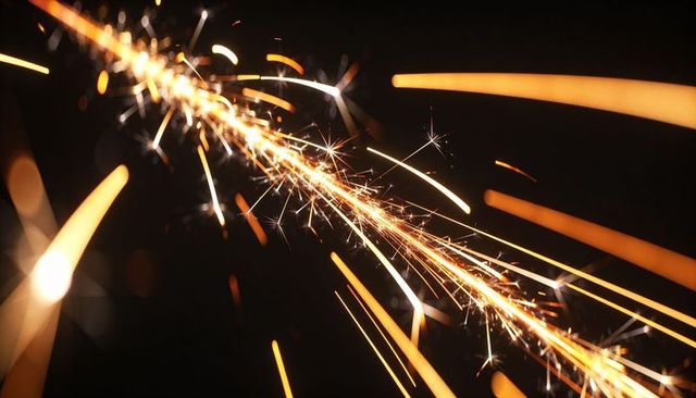 Sparkler streaking diagonally across dark background with golden sparks and bokeh trails