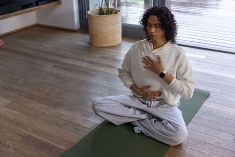 Nonbinary person meditating at home on green yoga mat practicing mindfulness and breathwork