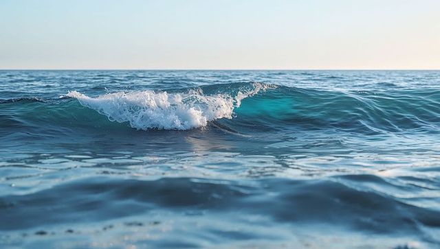 Turquoise ocean wave breaking with white foam and sunlight reflections at horizon, seascape