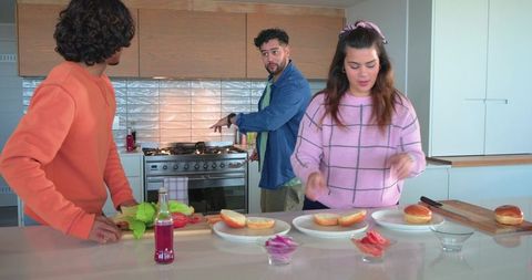 Multicultural friends preparing sandwiches on bright modern kitchen island with stainless range