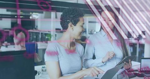 Women collaborating over tablet and laptop in modern office with pink data overlay