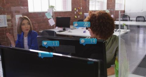 Coworkers collaborating across monitors and glass partition with social media notification overlays