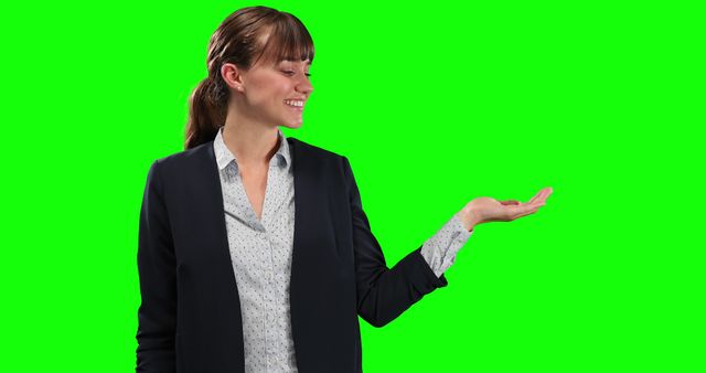 Smiling businesswoman dressed in professional attire, holding out hand with green screen background. Perfect for use in advertisements, client presentations, promotional materials, and web graphics. Ideal for creating customized content by adding text or other images in the blank space provided by the outstretched hand.