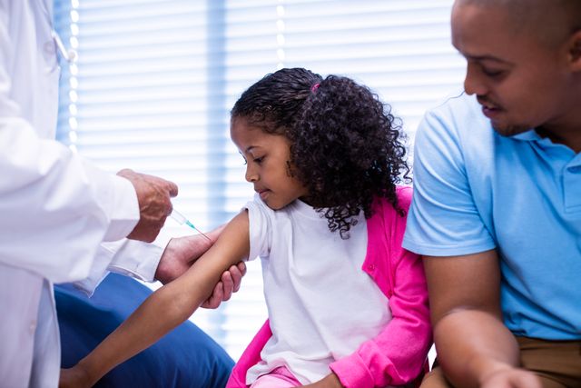 Doctor administering vaccine to young girl while her father watches. Ideal for use in healthcare, medical, and family-related content. Can be used to promote immunization, pediatric care, and health awareness.