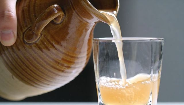 Pouring pale amber juice from ridged ceramic pitcher into clear glass with bubbles