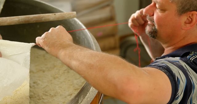 Baker checking consistency of dough in a large industrial mixer. Ideal for representing traditional bakery work, food preparation process, and culinary arts. Suitable for use in advertising for local bakeries, instructional cooking material, and articles on traditional baking techniques.