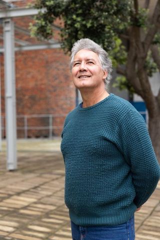 Thoughtful senior man in teal sweater looking upward in urban courtyard with brick backdrop