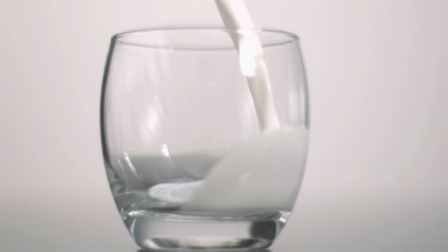 Milk smoothly pouring into a transparent glass depicts freshness and purity. Ideal for use in marketing related to beverages, dairy products, or nutrition, emphasizing health and freshness. Useful for advertisements, healthy lifestyle guides, and educational materials in food sciences.