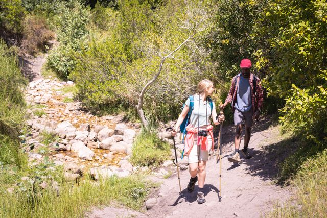 Diverse couple with backpacks walking on sunny day. Spending quality time, lifestyle and camping concept.