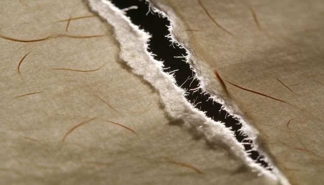 Torn handmade paper with frayed fibers revealing dark gap macro texture background