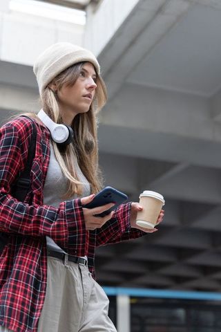 Young commuter standing under concrete grid ceiling holding coffee and smartphone