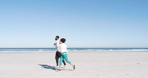 Diverse friends jogging on empty beach in hoodies and sneakers casting long shadows
