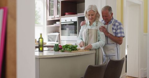Senior couple joyfully cooking together at home kitchen