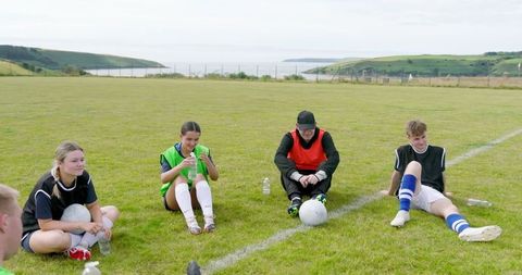 Teen Soccer Team Resting on Scenic Coastal Field After Practice