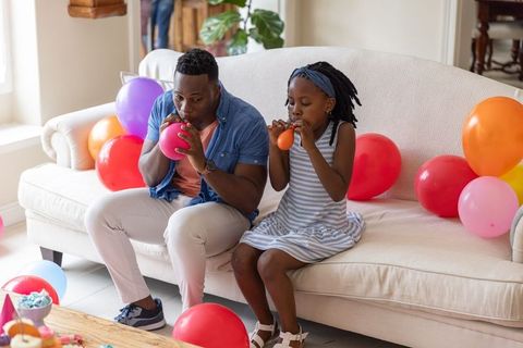 African american father and daughter inflating colorful balloons for home birthday party