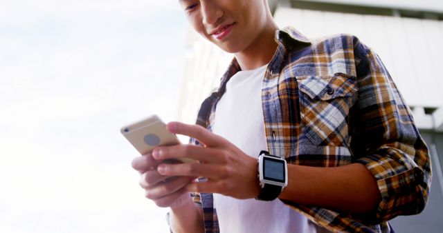 Young man engaged with smartphone while wearing casual attire. Suitable for technology, lifestyle, or youth culture topics. Ideal for illustrating modern communication, urban trends, and tech-savvy demographics.