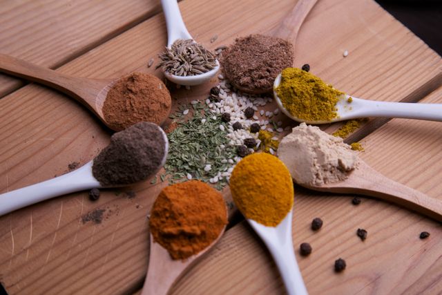 Various spices and herbs are displayed in a visually pleasing arrangement using wooden and porcelain spoons. Perfect for use in food blogs, culinary articles, cooking magazines, restaurant menus, and as kitchen wall art. Showcases concepts of diversity in flavors and food preparation.