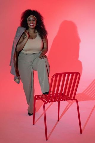 Confident african american woman smiling, posing with blazer over shoulder on red