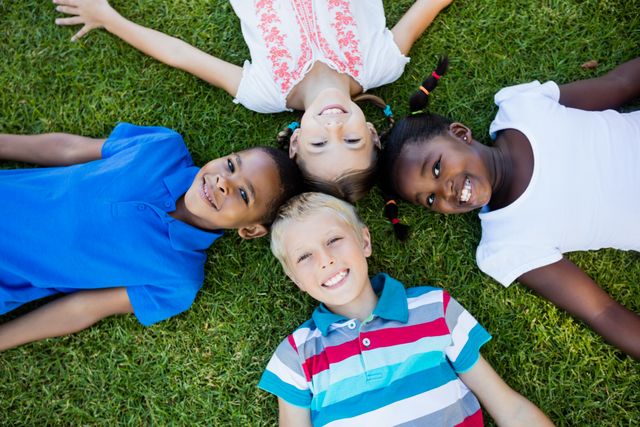 This image shows a diverse group of happy kids lying on the grass in a park on a sunny day. They are smiling and enjoying each other's company, showcasing friendship and togetherness. This image can be used for promoting outdoor activities, childhood joy, diversity, and community bonding. Ideal for educational materials, advertisements for children's products, and social campaigns focused on inclusivity and play.