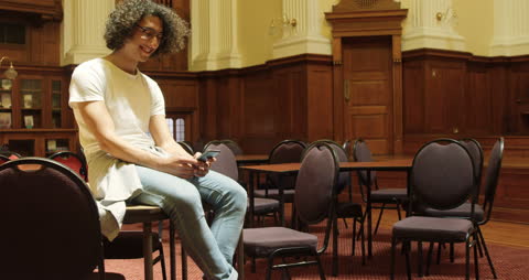 Smiling Young Man Using Smartphone in Vintage Library