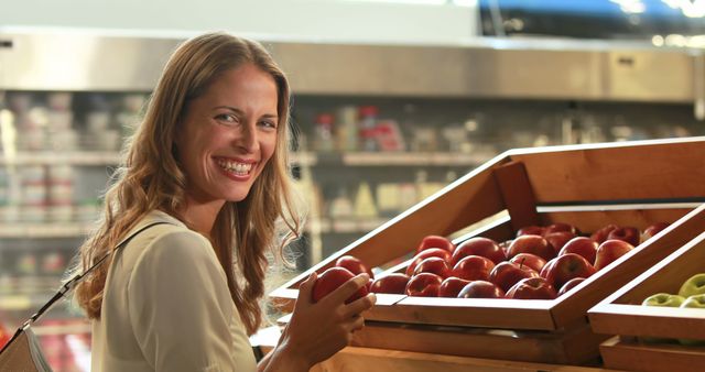 Woman enthusiastically selecting fresh apples in supermarket produce section. Ideal for topics on healthy eating, grocery shopping, nutrition, happy customers, and organic produce. Perfect for advertising retail grocery stores, wellness blogs, and nutritional content.