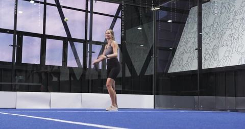 Female athlete serving on indoor padel court with glass walls and minimalist mural