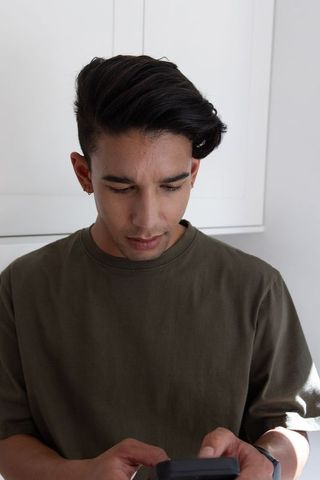 Asian man checking smartphone in kitchen wearing olive crewneck and hoop earrings