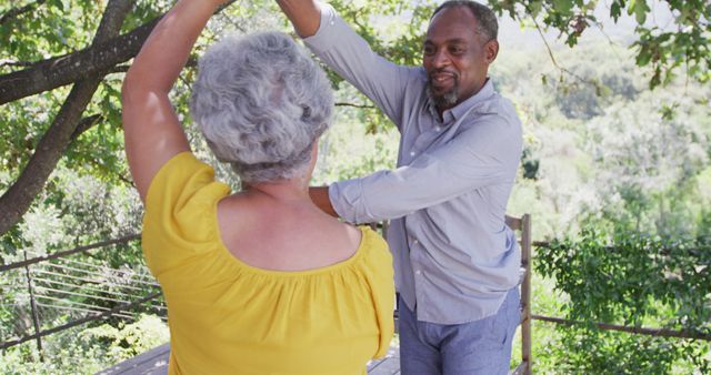 Happy senior biracial couple having fun dancing together in sunny garden smiling. Senior lifestyle, nature and togetherness.