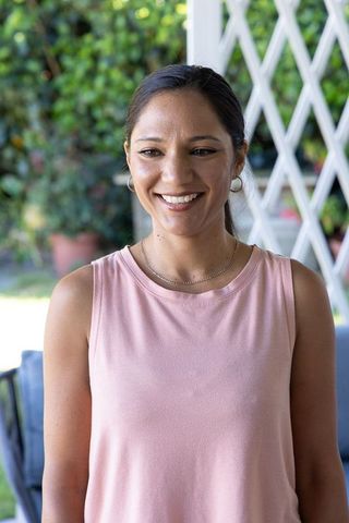 Smiling woman on porch in pink sleeveless top with hoop earrings, casual outdoor portrait