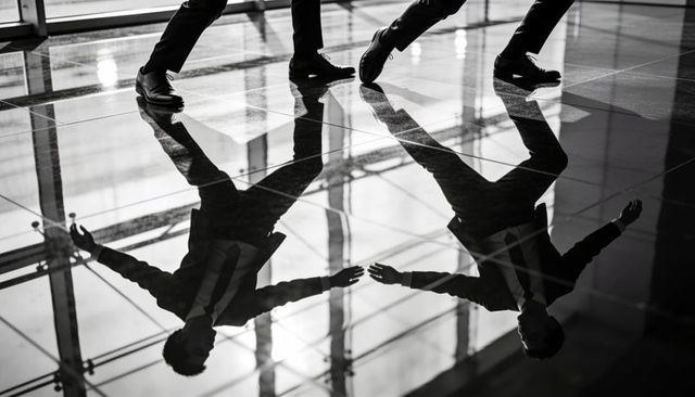 Businessmen walking across glossy lobby floor with dramatic reflections and long shadows