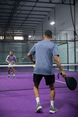 Padel player returning ball on indoor purple court, paddle swing and net play