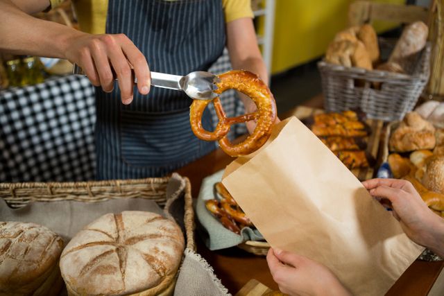 Mid section of staff packing pretzel bread in paper bag at counter in bakery shop