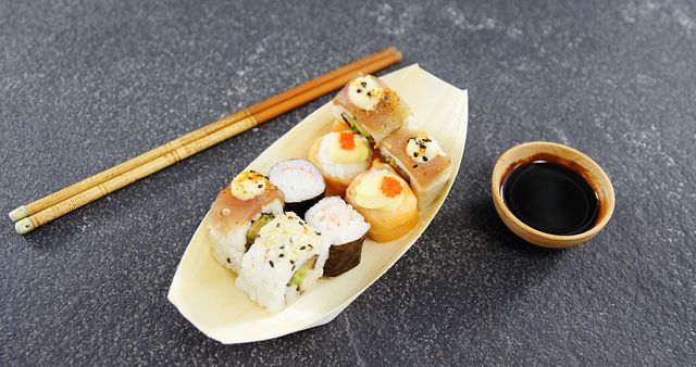 A variety of sushi rolls are neatly arranged on a wooden plate, accompanied by chopsticks and a small bowl of soy sauce, with copy space. Sushi, a traditional Japanese dish, is often enjoyed for its fresh flavors and artistic presentation.