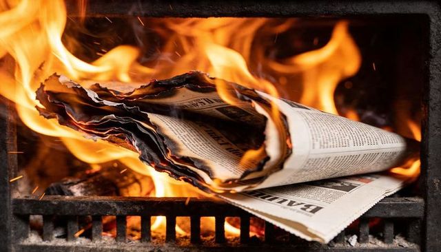Burning newspaper curling and charring on metal grate with flames and glowing embers