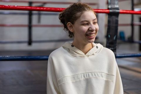 Smiling teenage female training in boxing ring wearing cream hoodie, confident portrait