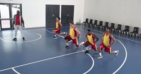 Basketball coach training team with lunges on indoor court