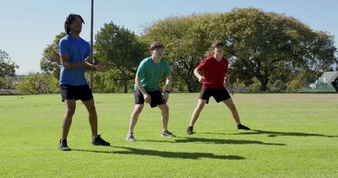 Sunlit team warmup: three athletes squatting and clapping on grass during training drill