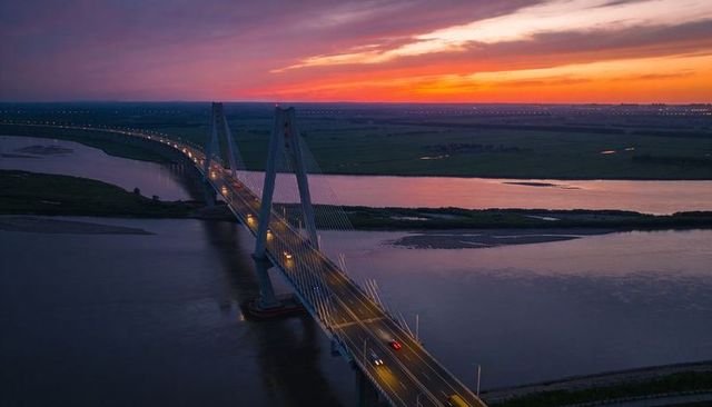 Cable-stayed bridge crossing river at sunset with twin towers reflecting on water