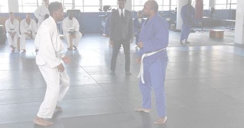 Sparring martial artists wearing white and blue gis on dojo mats practicing combat training