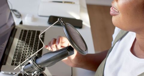African american woman podcasting with microphone and laptop at home office