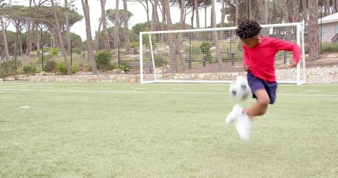 Boy Skillfully Kicking Soccer Ball on Field in Red Shirt