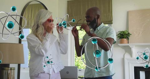 Senior couple interacting with augmented reality atom models in home with laptop, red glasses