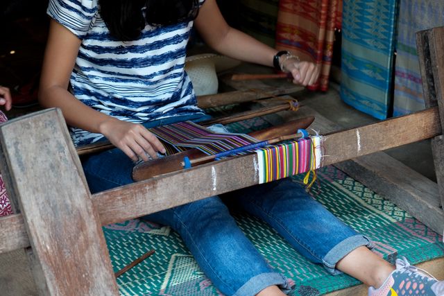 Woman engaged in traditional weaving using a wooden loom, showcasing the intricate process of creating handmade textiles. Ideal for illustrating topics on traditional crafts, cultural heritage, DIY projects, and artisan communities.