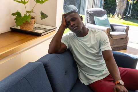 African American man relaxing on blue couch gazing through sliding glass doors in modern home