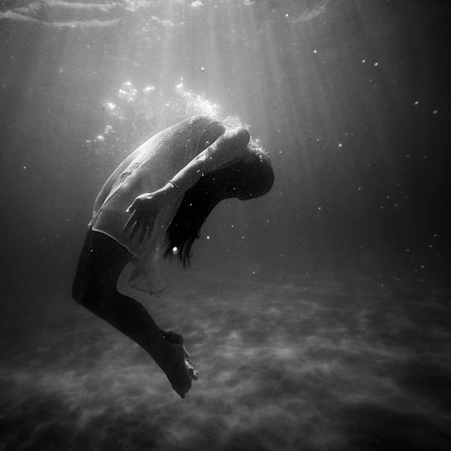 Underwater shot of a woman in a flowing dress, creating a serene and ethereal scene. Rays of light penetrating the water surface add a mystical touch. Ideal for concepts of tranquility, introspection, and surreal photography. Suitable for use in artistic projects, therapeutic content, or editorial spreads on mental health and relaxation.