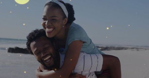 Young couple sharing piggyback laughter on sunlit beach with golden sparkle overlay