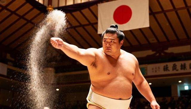 Sumo wrestler throwing ceremonial salt before match in traditional dohyo under japanese flag