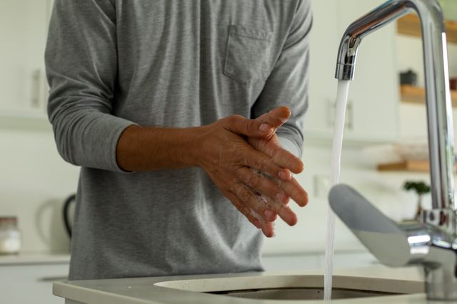 Caucasian father washing his hands in the sink at home. he's soaping his hands before rinsing it with water from the faucet.