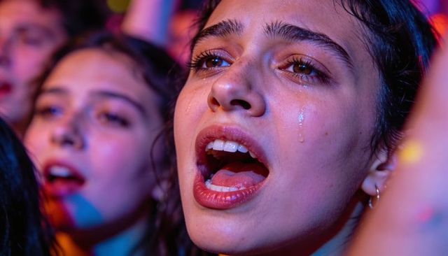 Closeup of emotional concert fan singing and crying under neon stage lights